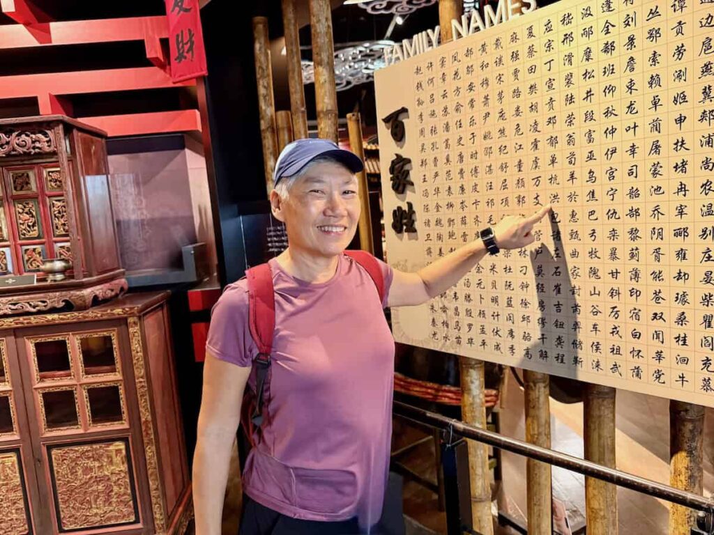 Reggie pointing to her family name on a wall with Chinese characters at the Chinese Museum in Kuching.